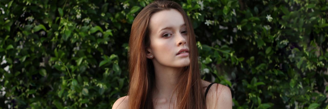 'High-Functioning' Anxiety Doesn't Mean It's Any Less Severe young woman with brown hair in front of green bushes looking at the camera with a straight face