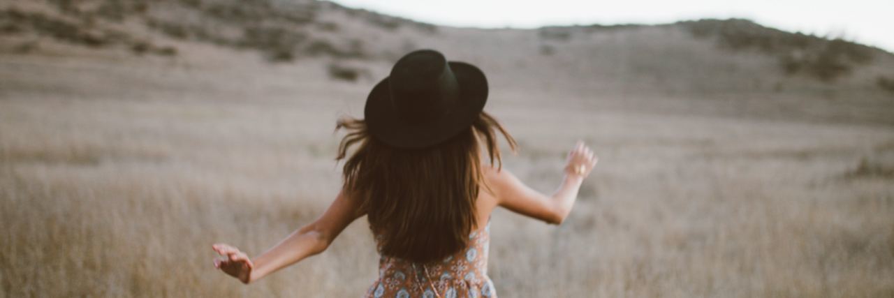 What I Do to Start My Week With Less Anxiety Woman in a black hat and romper dancing through a field, back of woman