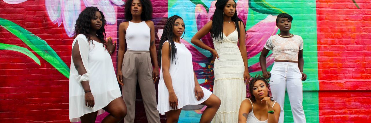 How People of Color Describe Their Experience With Trauma and Stigma photo of group of women of color against brightly colored wall mural with flowers and leaves