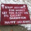 Red and white sign that reads: "Stop asking for money. Let the baby die. It's called Darwinism. Happy Holidays"