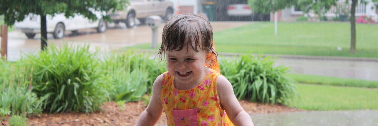 Child wearing an orange dress, dancing in the rain.