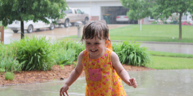 Child wearing an orange dress, dancing in the rain.