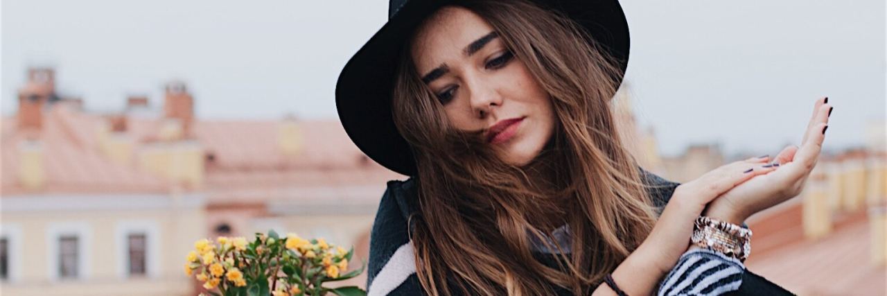 How Falling Into the ‘Comparison Trap’ Impacts Your Mental Health woman in a city sitting at a table in a black hat with long brain hair looking down