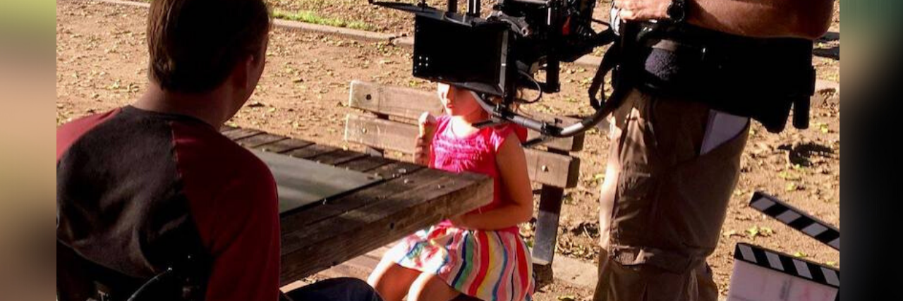 New Film 'Daruma' Stars Actors With Real Disabilities Tobias Forrest and a young girl on the set of Daruma with a camera pointed at Tobias. Logo for Daruma in bottom right.