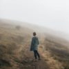 photo of woman standing facing away from camera on foggy path