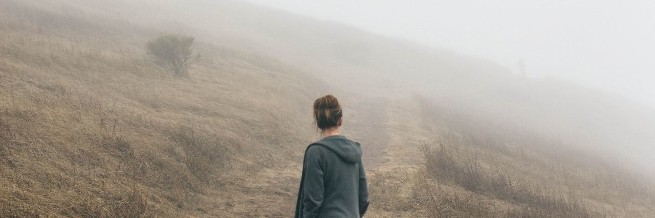 photo of woman standing facing away from camera on foggy path