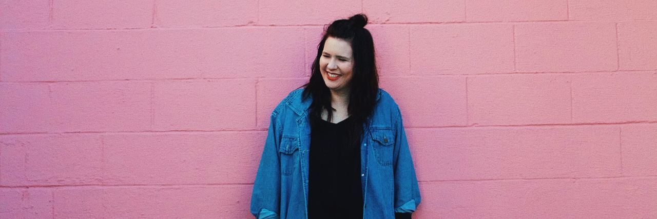 How I Found Body Neutrality in My Self-Image This Year photo of woman standing against pink wall and smiling or laughing