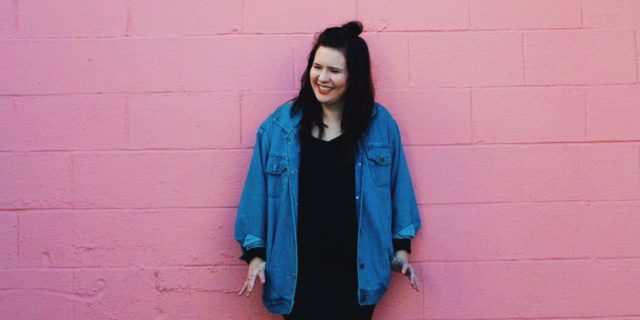 photo of woman standing against pink wall and smiling or laughing