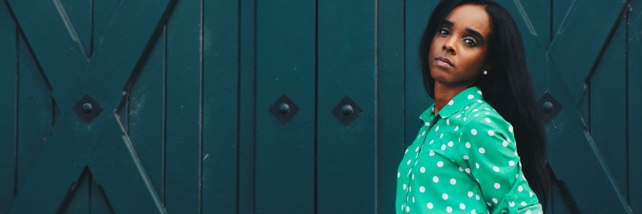 Why Setting Boundaries Is Important for Your Health at Thanksgiving photo of woman standing in front of teal colored wooden doors with hands in skirt pocket