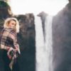 woman standing in front of a waterfall with a blanket wrapped around her