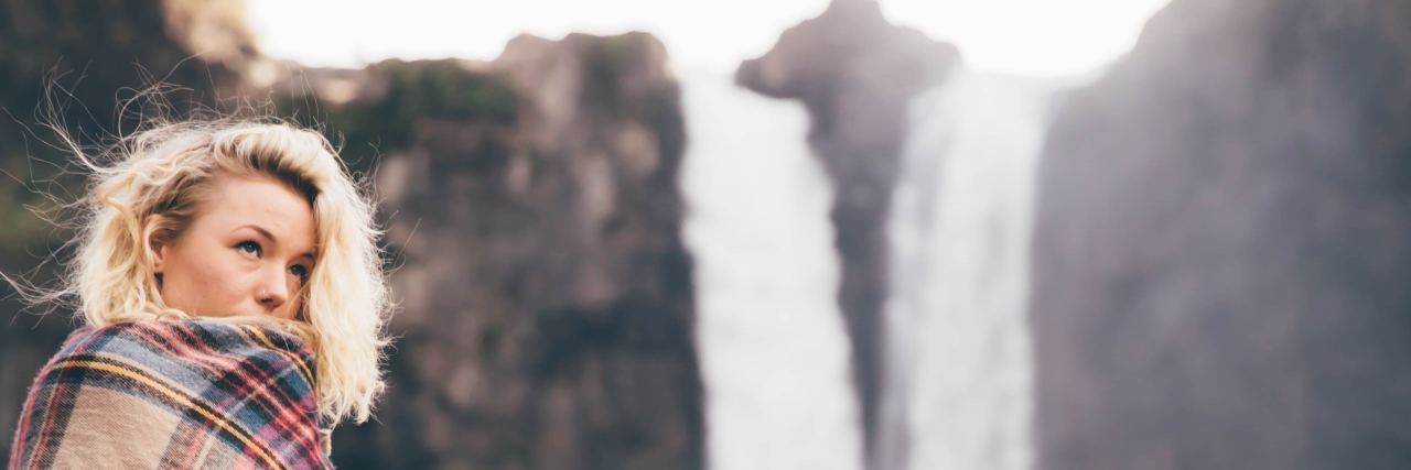 How I'm Finding Confidence Again With Functional Neurological Disorder woman standing in front of a waterfall with a blanket wrapped around her