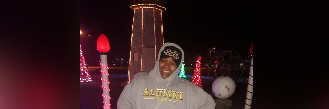 Surviving the Holidays as a Chronic Illness Warrior Jae posing outside with Christmas lights.