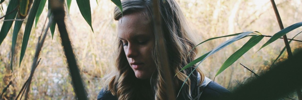 What It's Like to Live With Catastrophic Thoughts artsy shot of a woman in a jungle/forest looking down between trees