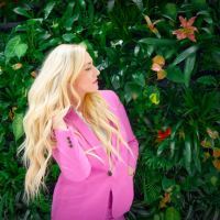 photo of blonde woman standing in front of greenery with eyes closed