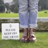 person standing next to a sign saying please keep off the grass