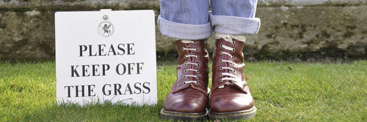 person standing next to a sign saying please keep off the grass