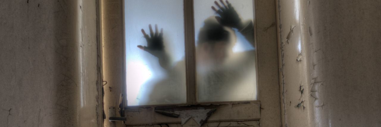 'Bipolar Exhaustion' Makes Me Feel Fatigued Like a Zombie photo of man silhouetted behind frosted glass of old wooden door in abandoned building