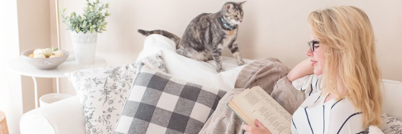 photo of woman sitting at home reading book with cat