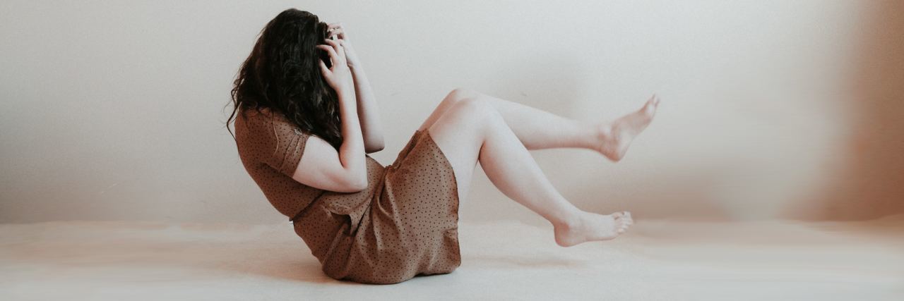 'Simple' Ways to Practice Self-Care on Bad Mental Health Days photo of woman in crunch position with head in hands looking pained or upset