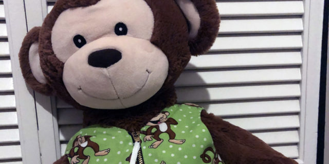 A picture of a big stuffed monkey wearing a green vest.