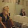 photo of young woman sitting in bathroom on sink looking at her reflection in mirror