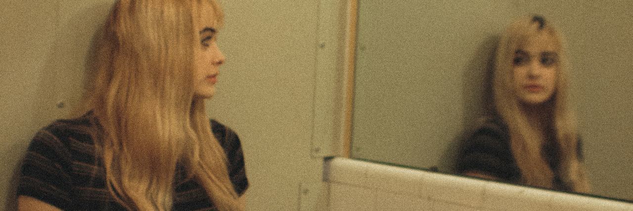 photo of young woman sitting in bathroom on sink looking at her reflection in mirror