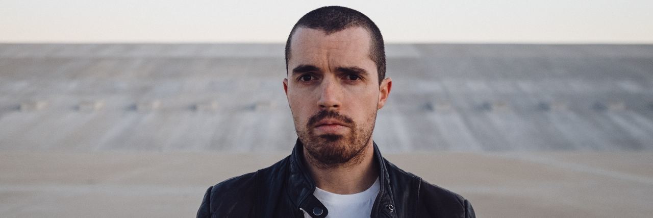 Why Comparing OCD Diagnoses Is Dangerous and Unhelpful photo of a man in a black leather jacket with a white t shirt staring into the camera with a serious face