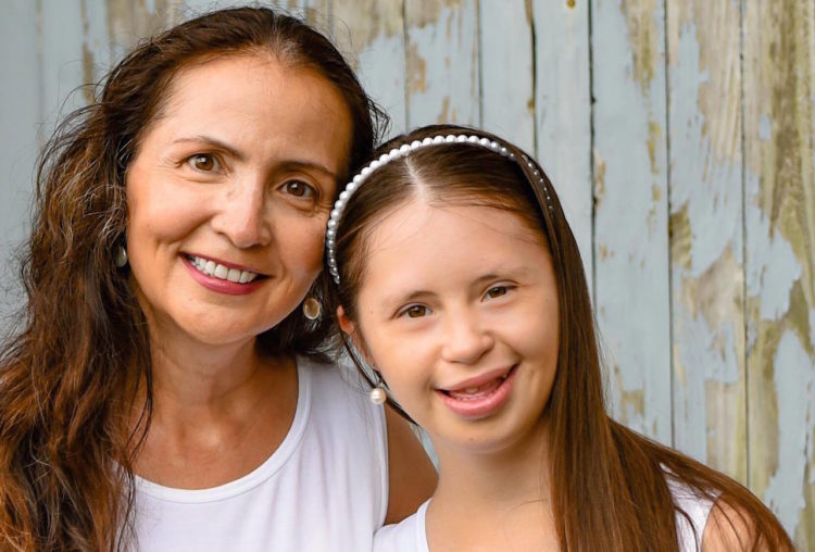 The author and her daughter, who has Down syndrome. Their both smiling and wearing white. They both have brown hair. 