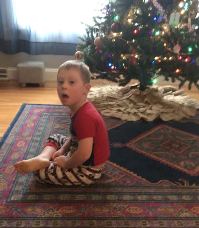 a boy in Christmas pajamas sitting near the Christmas tree