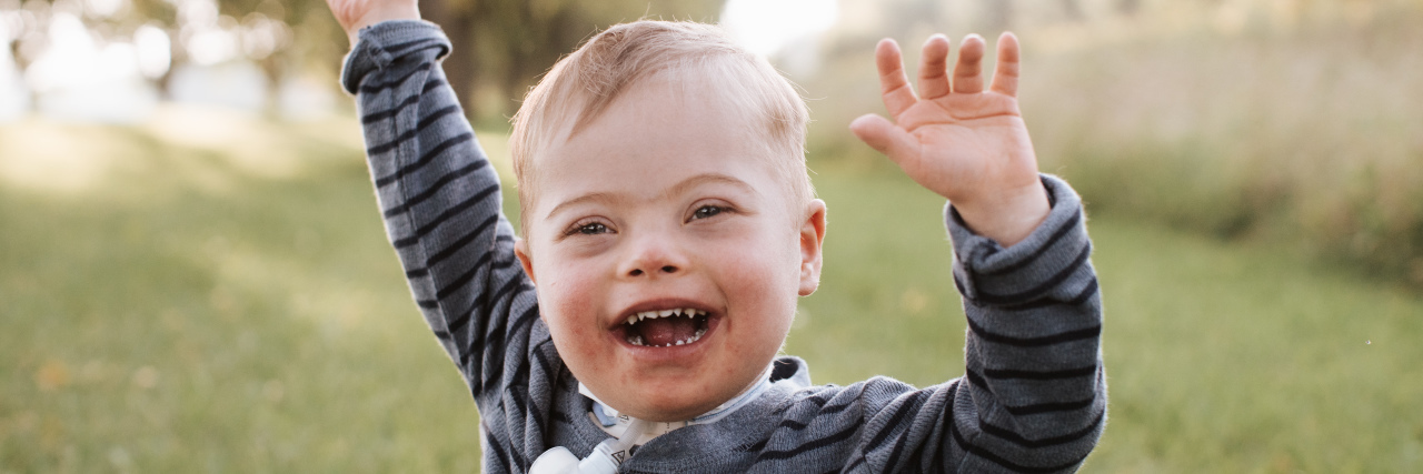 Amber's son AJ, who has Down syndrome and a tracheostomy, laughing outdoors.