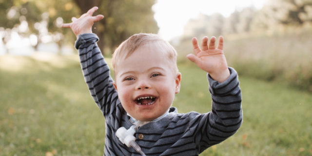 Amber's son AJ, who has Down syndrome and a tracheostomy, laughing outdoors.