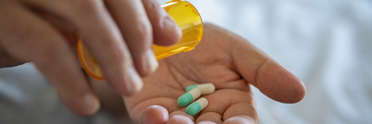 I'm Thankful for My Antidepressant, but Not Its Withdrawal Symptoms person's hand pouring three green and white capsule pills into the other hand