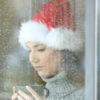 A woman looks solemnly out of a rainy window wearing a Christmas hat.