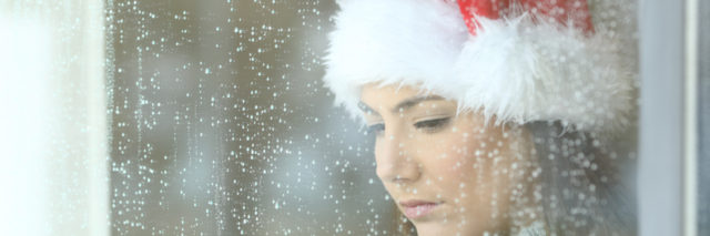 A woman looks solemnly out of a rainy window wearing a Christmas hat.