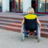 Woman in wheelchair sitting in front of stairs.