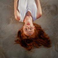 woman with red hair wearing a white shirt lying down on a beach with her eyes closed