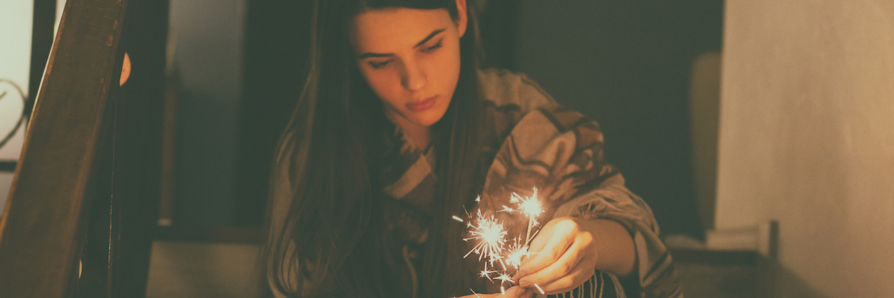 A young woman sitting on steps in the dark holding sparklers
