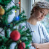 woman leaning against window sad, looking at christmas tree