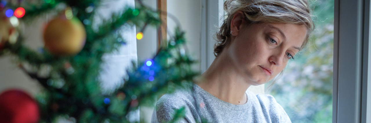 woman leaning against window sad, looking at christmas tree