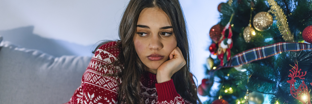 A Migraine Specialist on Coping With Migraine During the Holidays Lonely women sitting on the the sofa at home during christmas.