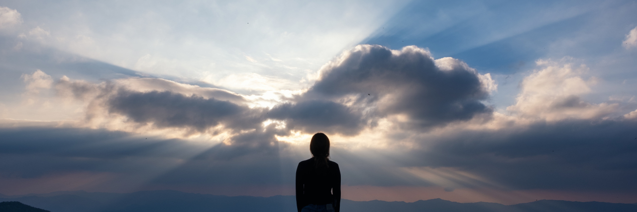 Woman standing and watching sunset with mountain view.