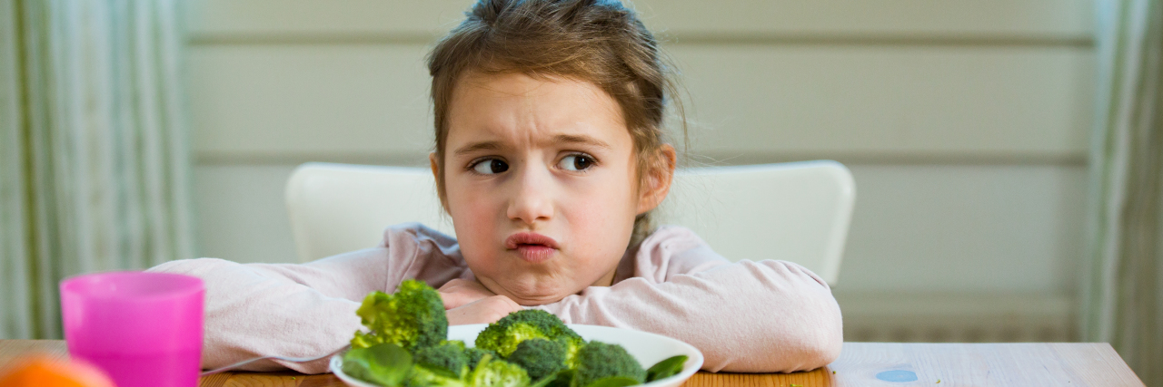 Unhappy girl eating spinach and broccoli at the table.