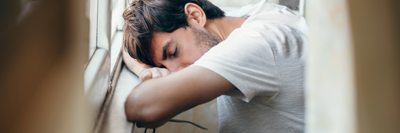 3 Things I Want You to Know About Tics and Tourette Syndrome a young man lying his head on a window seal with his glasses in his hand