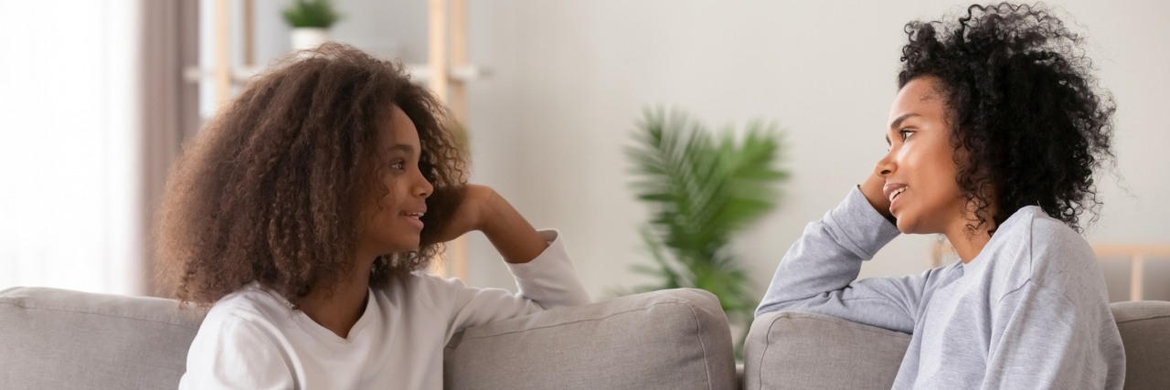 How to Talk to Someone About Their Cancer Journey Young african black mother chatting with teen daughter, older sister or friendly nanny and adolescent girl talking sitting together on sofa at home. Good relations different aged people trust concept