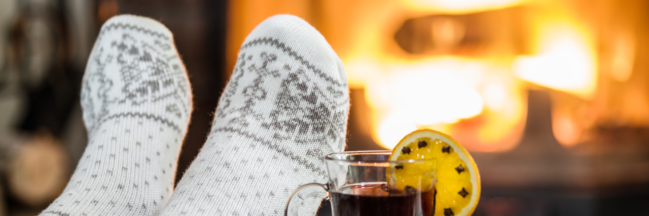 5 Great Gifts for Someone With Chronic Foot and Ankle Pain Woman wearing fuzzy socks relaxing by fireplace.
