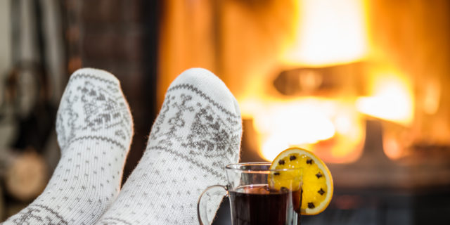 Woman wearing fuzzy socks relaxing by fireplace.
