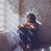 woman sitting in bed with head in knees, light coming through window