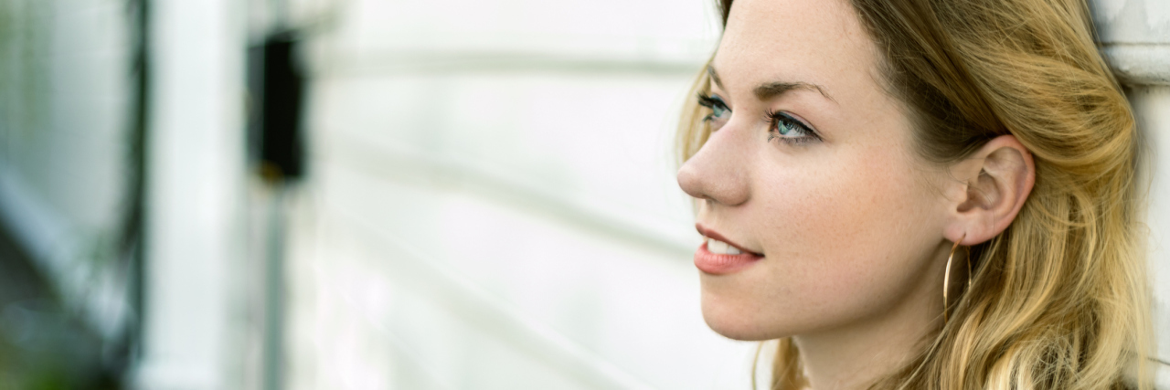 What It's Like Being Hard-of-Hearing Portrait of a blonde young woman with blue eyes, profile view, looking away, pensive, dreaming, over an street background, outdoors.