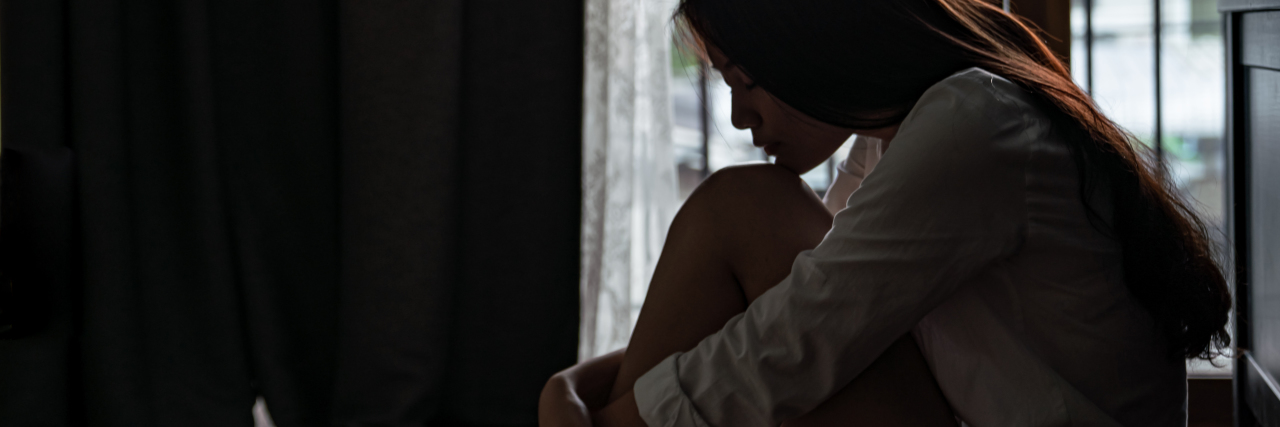 Woman sitting in a dark room holding her knees.