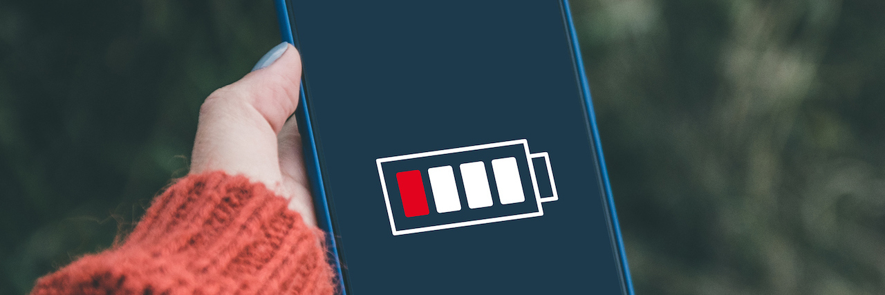 Trying to Describe What Chronic Illness Feels Like Close-up view of hand holding a smartphone with low battery on screen.